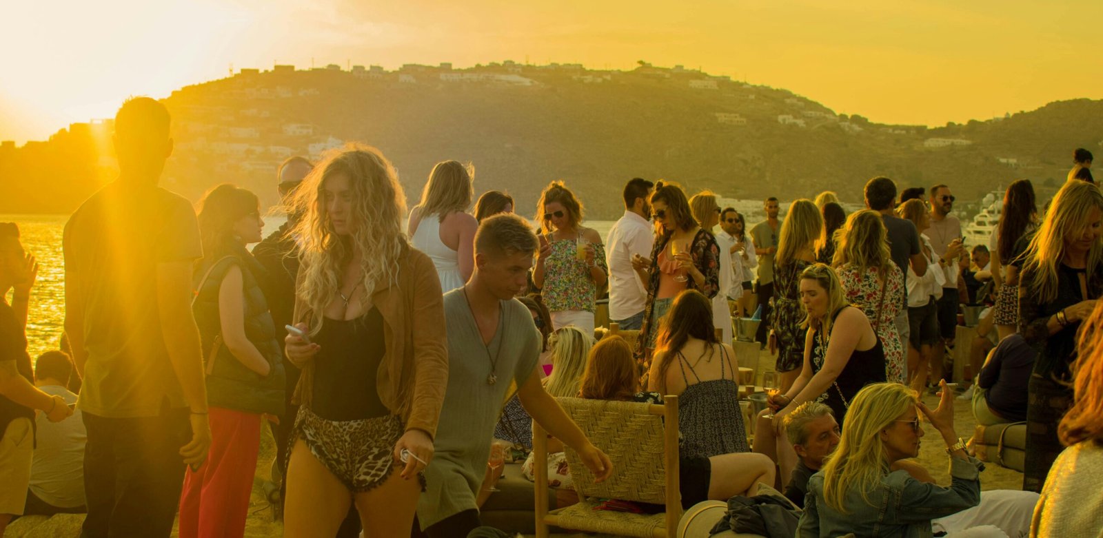 A lively gathering of people enjoying a sunset party on a beach in Mykonos, Greece.